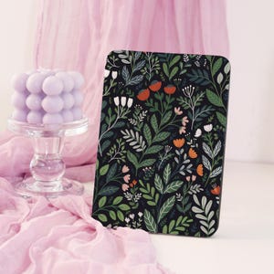 May include: A black rectangular case with a floral pattern featuring red, orange, white, and green leaves and flowers. A lavender bubble candle sits on a clear glass pedestal, with pink fabric in the background.