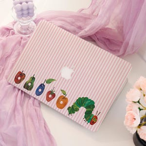 May include: A laptop skin featuring a light pink and white vertical striped pattern. The design includes a series of colourful fruit illustrations, including an apple, pear, plum, strawberry, and orange, followed by a green caterpillar character.