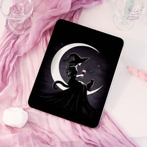 May include: Black tablet case featuring a witch silhouette on a crescent moon with a black cat. The witch is holding a glass of red wine. The background is a starry night sky.