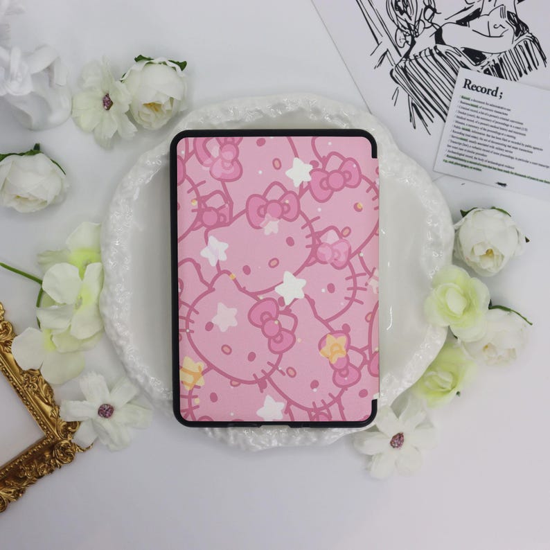 May include: Pink tablet case featuring a repeating pattern of Hello Kitty faces, bows, and stars. The case has a black border and is surrounded by white flowers and a decorative plate.