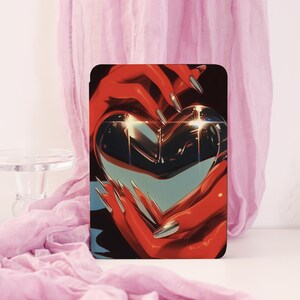 Könnte beinhalten: Eine schwarze Tablet-Hülle mit einem herzförmigen Design. Das Kunstwerk zeigt rote Hände mit langen, silbernen Nägeln, die ein reflektierendes, metallisches Herz halten. Der Hintergrund ist ein Farbverlauf aus Schwarz, Blau und Weiß, mit rosa Stoff im Hintergrund.