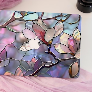 May include: A laptop skin featuring a stained-glass floral design. The design showcases large, stylized magnolia flowers in shades of pink, purple, and blue, with a white Apple logo visible. The skin has a glossy finish and a dark outline.
