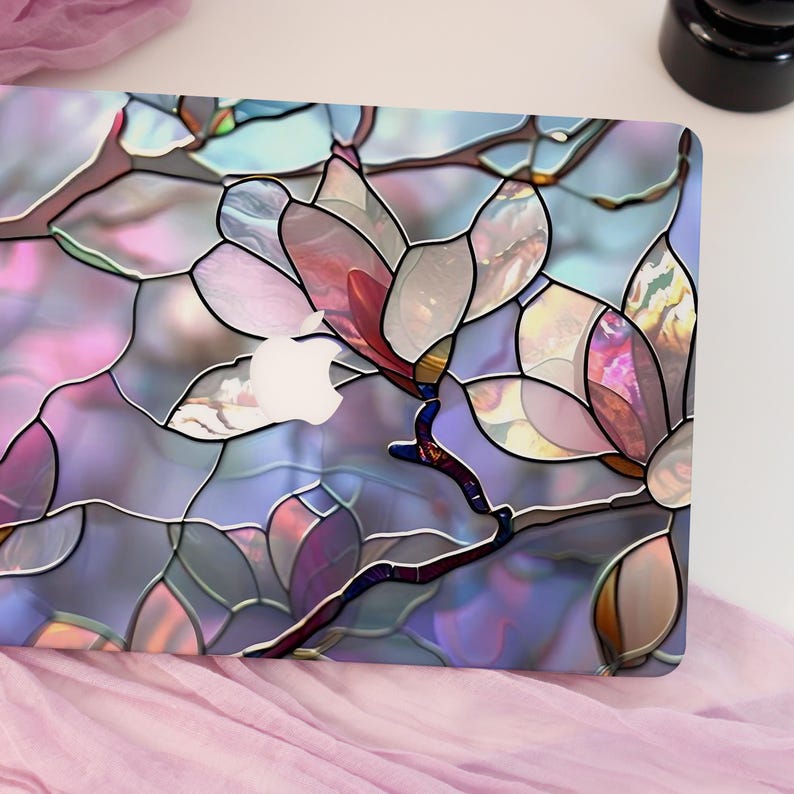 May include: A laptop skin featuring a stained-glass floral design. The design showcases large, stylized magnolia flowers in shades of pink, purple, and blue, with a white Apple logo visible. The skin has a glossy finish and a dark outline.