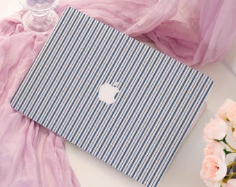 Może przedstawiać: Laptop z niebiesko-białym wzorem w paski. Laptop ma białe logo Apple na obudowie. Tło obejmuje różowy szalik, szklany świecznik z fioletowymi świecami i bukiet różowych kwiatów.