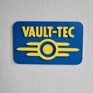 Może przedstawiać: Niebieski prostokątny znak z żółtym napisem "VAULT-TEC". Poniżej żółte koło z trzema poziomymi żółtymi liniami po każdej stronie. To przedmiot o tematyce gier.
