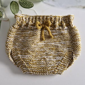 Peut inclure: Une paire de bloomers pour bébé en tricot à rayures jaunes et blanches. Les bloomers ont une taille à cordon avec un nœud papillon.