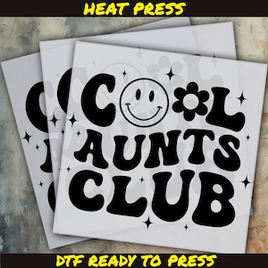 May include: Three white DTF (Direct to Film) transfer sheets with the text "COOL AUNTS CLUB" in black, featuring a smiley face and a flower. The words "HEAT PRESS" and "DTF READY TO PRESS" are also visible.