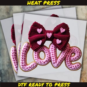 May include: A design featuring a burgundy bow with pink heart accents and the word "LOVE" in pink, outlined in gold. The text "HEAT PRESS" and "DTF READY TO PRESS" are displayed in yellow.