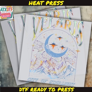Puede incluir: Hojas de transferencia DTF (Directo a Película) blancas apiladas con un diseño colorido. El diseño presenta la palabra "VELARIS" en una fuente holográfica, una luna creciente, estrellas y una cordillera. También se ve el texto "CITY OF STARLIGHT".