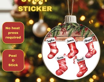 May include: A round Christmas ornament sticker with a festive design. It features five red and white stockings, each with a name, set against a wooden background with greenery. The text "UV DTF STICKER" is at the top.