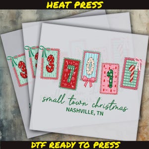 May include: A stack of white DTF (Direct to Film) transfer sheets with Christmas-themed designs. Each sheet features a numbered design in a decorative frame, with the text "small town christmas" and "NASHVILLE, TN". The top of the image reads "HEAT PRESS".