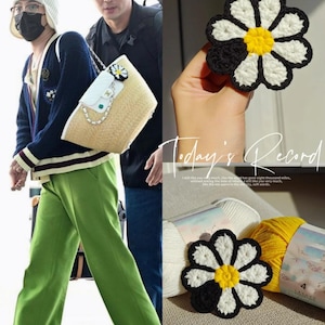 May include: A crochet daisy flower with black, white, and yellow petals. The flower is handmade and appears to be part of a larger craft project. The image also shows a straw handbag with a daisy embellishment.