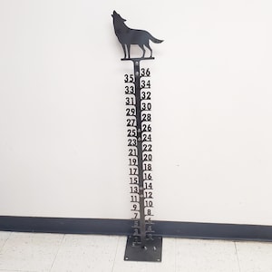 May include: A black metal height chart featuring a wolf silhouette at the top. The chart has numbers from 1 to 36 printed on it.