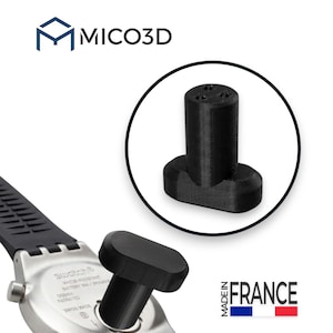 Puede incluir: Una herramienta negra impresa en 3D para la tapa de la batería de un reloj Swatch. La herramienta presenta una parte superior cilíndrica con tres pequeñas hendiduras y una base ovalada. El texto MICO3D es visible arriba y MADE IN FRANCE abajo.