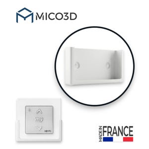 Op de afbeelding: Een witte kunststof wandhouder voor een afstandsbediening, voorzien van twee schroefgaten. Een vierkante afstandsbediening met knoppen voor omhoog, omlaag en my is in de houder geplaatst. Het MICO3D-logo en de tekst Made in France zijn zichtbaar.