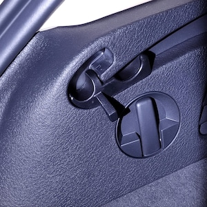 Puede incluir: Primer plano del interior de un coche azul oscuro con una superficie texturizada. La imagen presenta una palanca de plástico negro y un mando circular. La palanca está cerca de un asa curva, y el mando tiene un diseño rectangular.