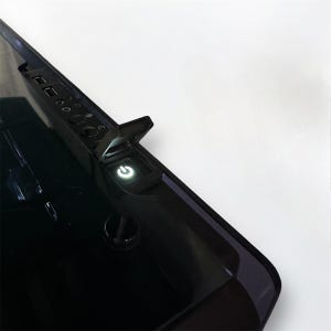 Peut inclure: Gros plan sur le bord inférieur d'un écran d'ordinateur noir, avec un bouton d'alimentation vert lumineux. L'écran a une finition brillante et comprend des ports USB et d'autres options d'entrée.