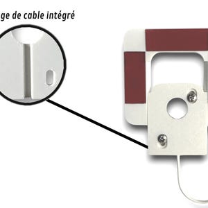 May include: A white, square-shaped device with a rectangular opening and a circular hole. It has four red squares on the corners and a white cable with a USB connector. The text "Passage de cable int&eacute;gr&eacute;" is visible.