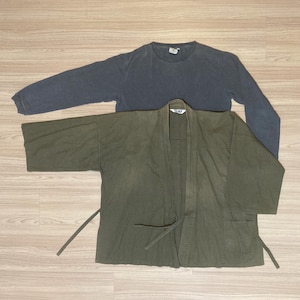 May include: A dark green hemp jacket with a tie belt and a pocket on the left side. The jacket is layered over a long-sleeved, dark blue shirt.