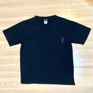 May include: A black V-neck t-shirt with a pocket on the left chest. The shirt has short sleeves and a small tag at the neckline. The pocket has a small white graphic. The shirt is made of a soft material.