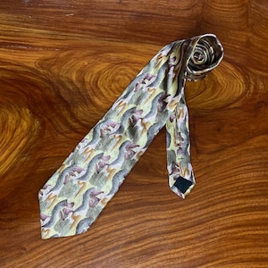 Può includere: Una cravatta fantasia con un motivo ripetuto di forme astratte nei toni del verde, marrone e viola. La cravatta è realizzata in un materiale setoso e viene esposta su una superficie di legno.