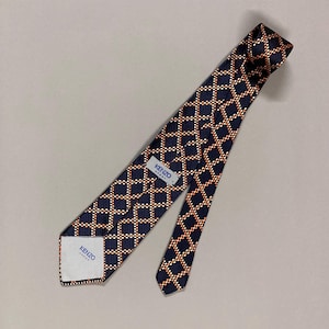 May include: A navy blue tie with a geometric pattern of orange squares and white dots. The tie has a label that reads "KENZO PARIS". The tie is made of a smooth fabric and is suitable for formal occasions.