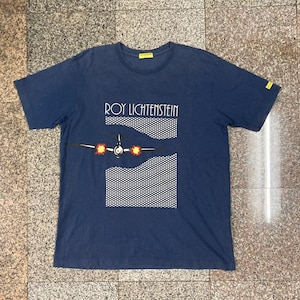 May include: A navy blue t-shirt with a white and black graphic of a plane with the text "ROY LICHTENSTEIN" printed on the front.