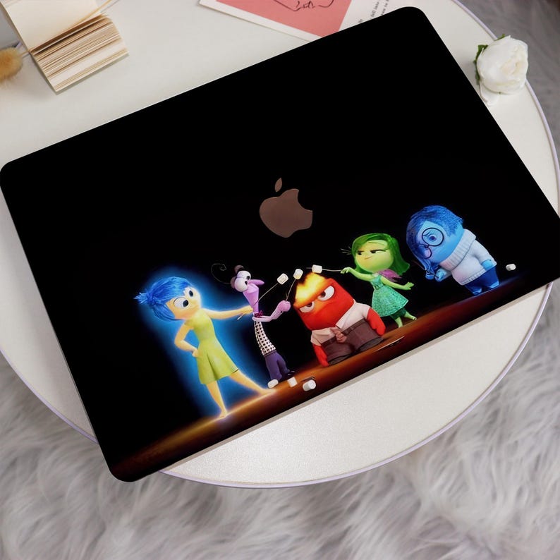 May include: A black laptop with a sticker of the characters from the movie Inside Out. The characters are Joy, Sadness, Fear, Anger, and Disgust. They are all standing in a line and are holding marshmallows on sticks. The laptop has a silver Apple logo on the back.