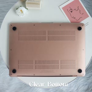 May include: The bottom of a rose gold laptop case with a clear bottom. The case has a textured surface and four small rubber feet.