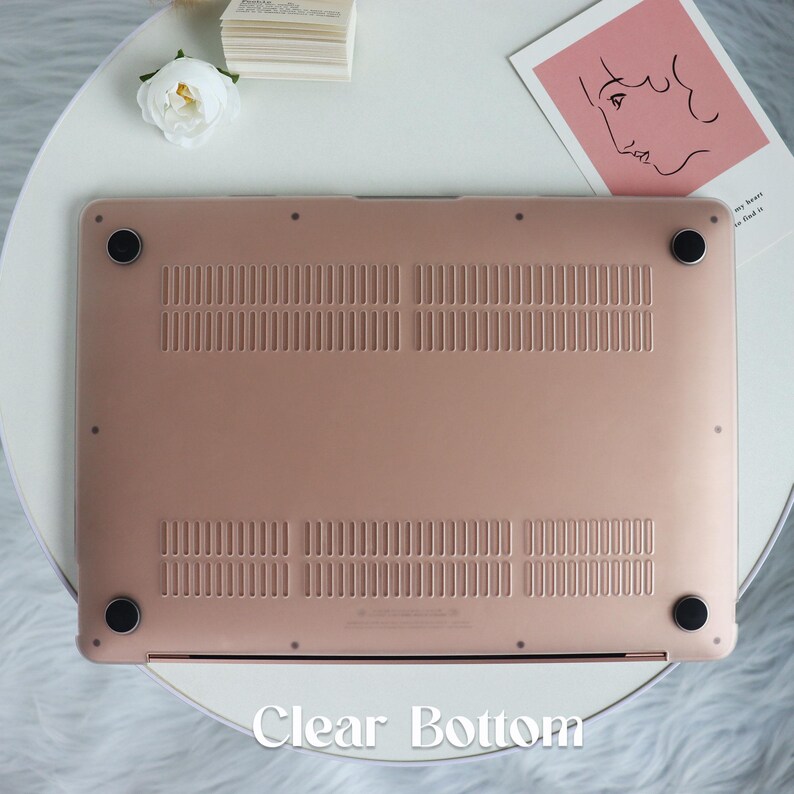 May include: The bottom of a rose gold laptop case with a clear bottom. The case has a textured surface and four small rubber feet.