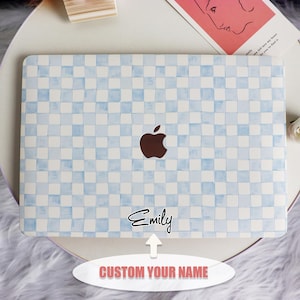 May include: A white laptop with a blue and white checkered pattern. The Apple logo is visible on the back of the laptop. The text "Emily" is written in black cursive on the bottom right corner of the laptop.