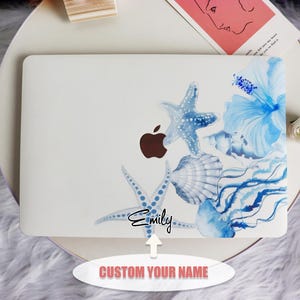 May include: White laptop skin with a watercolour design of blue starfish, seashells, and a hibiscus flower. The design includes the name "Emily" and the text "CUSTOM YOUR NAME". The Apple logo is visible.