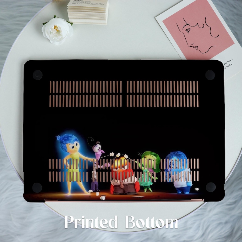 May include: A black laptop case with a printed image of five animated characters. The characters are blue, yellow, green, red, and purple. The characters are standing in front of a black background with a gold grid pattern. The text 'Printed Bottom' is printed in white on the bottom of the case.