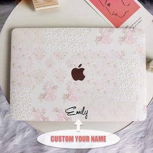 May include: A white laptop skin with a floral design in pink and white. The Apple logo is visible. The name "Emily" is written in black script. The text "CUSTOM YOUR NAME" is also visible.