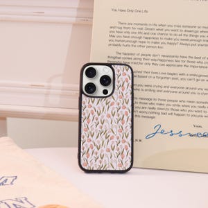May include: A black iPhone case with a floral pattern of pink and green flowers on a white background. The case has a black border and a camera cutout. The text on the paper says "You Have Only One Life".