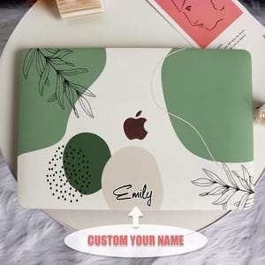 May include: A white laptop skin with a green, beige, and black abstract design. The design features leaves, circles, and dots. The skin has the word "Emily" written on it.