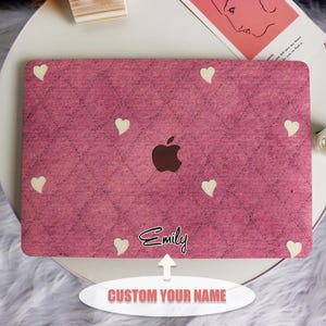 May include: Pink laptop case with a quilted design and white heart details. The case has a cutout for the Apple logo and the name "Emily" in cursive. The text "CUSTOM YOUR NAME" is also visible.