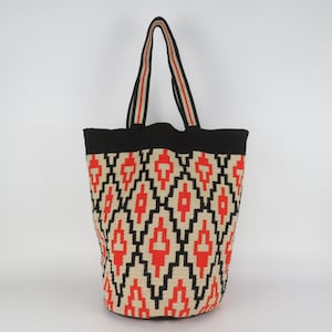 Peut inclure: Un sac fourre-tout tissé avec un motif géométrique rouge, noir et beige. Le sac a un dessus noir et des anses avec des rayures rouges et beiges. Conçu pour transporter des articles.