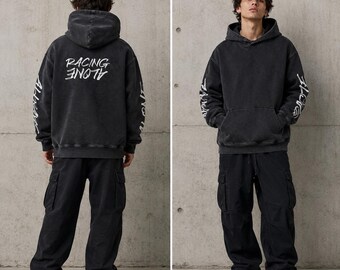 May include: A black hoodie with white text on the back that reads "RACING ALONE." The sleeves also have white text. The hoodie is paired with black cargo pants and white sneakers. The outfit has a casual, streetwear aesthetic.