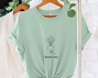 May include: A light green t-shirt with a black and white illustration of a beet and the text "beets me" printed on the front.