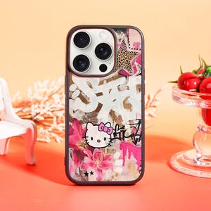 May include: A phone case featuring a Hello Kitty design with a graffiti-style background. The case has a black border and a colorful design with pink flowers, a leopard print star, and white graffiti-style text. The Hello Kitty character is in the lower center.