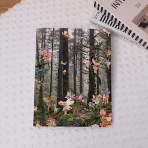 Könnte beinhalten: Ein Notizbuch mit einer Waldszene mit Feen, Schmetterlingen und Pilzen. Das Cover zeigt einen skurrilen Wald mit hohen Bäumen und einer Vielzahl farbenfroher Feenfiguren. Ein Buch mit dem Text "NEW Generation Graphics" befindet sich im Hintergrund.