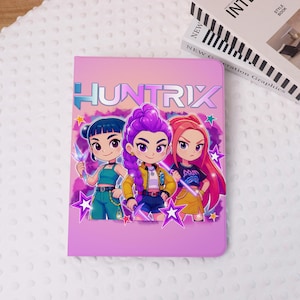 May include: A pink tablet case with the word "HUNTRIX" in blue and white. The case features a cartoon illustration of three girls with different hair colours, holding glowing objects. The background is a gradient of pink and purple.