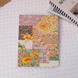 May include: A floral patterned notebook featuring a patchwork design with various flower illustrations in shades of orange, yellow, pink, and green. The notebook is rectangular and rests on a white, textured surface.