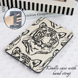 May include: A beige Kindle case with a black and white tiger print design. The case has a hand strap.