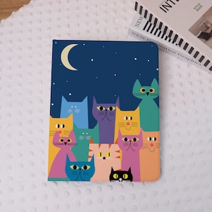 Puede incluir: Una colorida funda para tableta con una ilustración caprichosa de gatos bajo un cielo nocturno con una luna creciente y estrellas. Los gatos son de varios colores, incluyendo naranja, morado y azul.