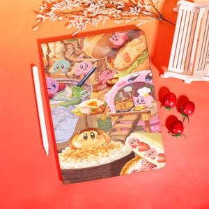 May include: A colorful notebook featuring a cartoon illustration of Kirby characters enjoying various foods. The design includes images of sandwiches, drinks, and other dishes. A white stylus rests on the side, with red and white decorative elements.