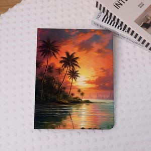Könnte beinhalten: Ein Notizbuch mit einer lebendigen Sonnenuntergangsillustration, die Palmen, eine Küstenlinie und eine Stadtsilhouette zeigt. Das Cover-Artwork verwendet eine warme Farbpalette aus Orange, Rot und Gelb, wobei das Meer den Sonnenuntergang widerspiegelt. Das Notizbuch ist rechteckig.