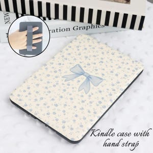 May include: Kindle case with a cream background and a blue floral pattern, featuring a light blue bow. The case has a black border and includes a hand strap for easy handling.