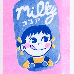 Op de afbeelding: Een illustratie van een blauw drankblikje op een roze achtergrond met de tekst Milky en Japanse tekens. Het blikje toont een stripfiguur met donker haar, een geel shirt en een blauwe tuinbroek, met de tong uit en roze wangen.
